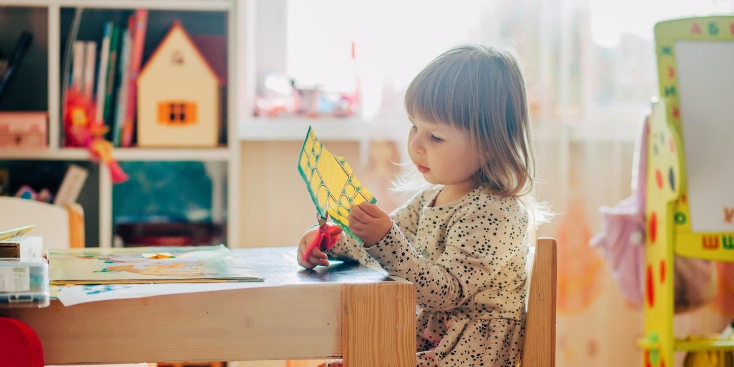 Preschool child cutting paper at desk